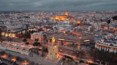 Seville old town with Torre del Oro tower, Cathedral and other historic buildings at night, Andalusia region, Spain. Aerial drone footage of Seville cityscape at night with street Illumination.