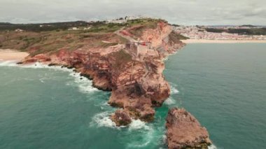 Portekiz 'in Nazare kasabasındaki Atlantik Okyanusu kıyısında bir kalesi olan uçurumun üzerindeki eski bir deniz fenerinin havadan görünüşü. Portekiz 'deki Nazare şehrinin yakınındaki deniz fenerine doğru uçuyor.. 