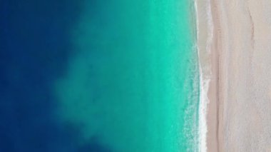 Aerial top down drone shot above an empty beach. The birds eye view of the amazing turquoise sea water and gentle waves crashing on an empty sand beach. Top down view over turquoise deep blue ocean