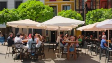 Geleneksel Avrupa açık hava kafesinin odaklı olmayan görüntüsü. İnsanlar güneşli bir yaz gününde Avrupa 'nın bilinmeyen bir şehrinde bir açık hava restoranında içiyor, yiyor ve sohbet ediyorlar. Bulanık gerçek zaman sahnesi