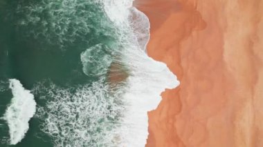 Top down view of ocean waves gently crashing on an empty sand beach. The birds eye view drone shot of large waves on the sand beach and dark ocean water. Portuguese sea coast. Still shot
