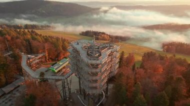 Güneş doğarken, tatil köyü Krynica-Zdroj 'daki ağaç tepesi gözlem kulesi, Küçük Polonya Voyvoda' sı. Tahta gözetleme kulesinin hava aracı yörünge görüntüsü, Krynica. Beskid Dağları 'ndaki sisli sabah manzarası