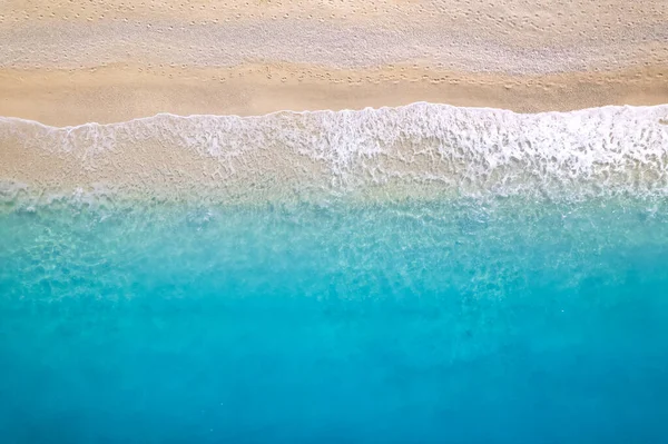 stock image Aerial top down drone shot above an empty beach. The birds eye view of the amazing turquoise sea water and gentle waves crashing on an empty sand beach. Top down view over turquoise deep blue ocean