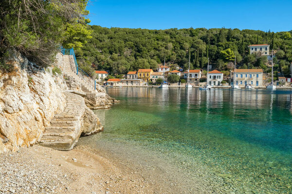 Небольшой пляж в рыбацкой деревушке Киони на острове Итака, Кефалония, Ионическое море, Греция. Лестница у моря в деревне Киони на Итаки. Все еще снят идиллический пейзаж греческого острова