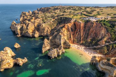 Portekiz 'in Algarve ilindeki Lagos kasabası yakınlarındaki Praia do Camilo plajı. Güneşin doğuşunda güzel Algarve sahili. Kayalık göldeki beyaz kumsalın havadan görünüşü.