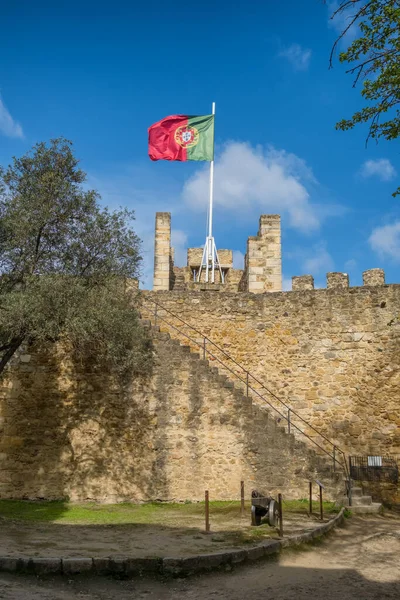Portugal national flag waving on ancient fortress wall of Sao Jorge Castle, at Moorish castle on highest hill in Alfama district. Lisbon Castle is a popular tourist attraction.