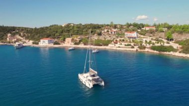Picoresque Fiskardo köyü ve Yunanistan 'ın Kefalonia adasındaki yelkenli katamaranın hava manzarası. Yunanistan 'ın Cefalonia kentindeki Fiscardo balıkçı köyüne demirlemiş yelkenli ve yatlar. Drone yörünge atışı