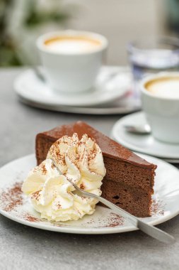 Avusturya, Viyana 'daki Cafe' de bir dilim Sacher Torte keki. Meşhur Avusturya çikolatalı sünger keki ve yakın plan kayısı reçeli. Arka planda buzlu kahve bardakları.