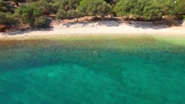Yunanistan 'ın Kefalonia kentindeki Chorgota plajında turkuvaz deniz suyunda yüzen bir kadının hava görüntüsü. Sefalonya adasındaki Horgota plajı. İHA videosu gösteriliyor