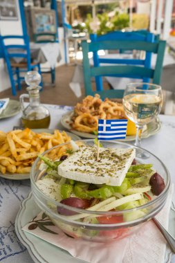 Taze Yunan salatası - beyaz peynir, domates, salatalık, kırmızı biber, siyah zeytin ve soğan. Yunan bayrağı üstte. Yunanistan 'da geleneksel taverna restautant' ında bir masaya yakın plan Horiatiki veya Köy salatası.
