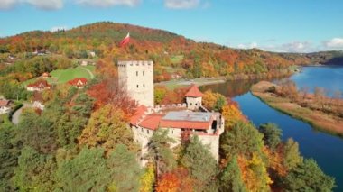 Medieval Tropsztyn castle in Lesser Poland Voivodeship by the Dunajec river, Poland. Aerial view of the historic castle on the bank of river in autumn. Orbit shot. National flag of Poland on the roof