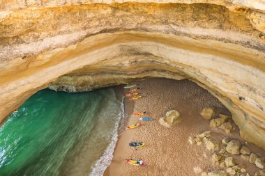 Benagil mağarası Lagos kasabası yakınlarında, Algarve bölgesi, Portekiz. Tanımlanamayan turistler mağaradaki Praia de Benagil plajına kadar kürek, SUP ve kanolarla yüzdükten sonra dinleniyorlar. Üst görünüm.