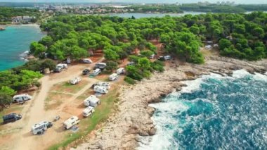 Hırvatistan 'ın Istria bölgesinin Pula kenti yakınlarındaki Adriyatik Denizi kayalık sahilinde park halindeki karavanları olan kamp alanının hava manzarası. Aile tatili karavanı, karavan tatili, karavan tatili..