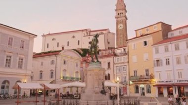 Piran, Slovenya - 17 Şubat 2023: Giuseppe Tartini heykeli, Piran 'ın eski kenti Tartini Meydanı' nda gün batımında, Slovenya. Aziz Georges Kilisesi ile Tartini Meydanı 'nın yavaş çekim görüntüleri.. 