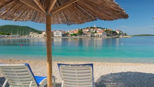 一个空旷的海滩 有一把遮阳伞 海滩上有两张空的日光浴床 克罗地亚迷人的普里莫斯滕镇和亚得里亚海的风景秀丽 一个理想的暑假旅游目的地 — 图库视频影像