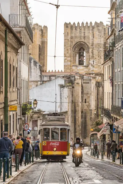 Lisbon, Portugal - March 27, 2022: Old portuguese retro tram with Lisbon cathedral at background in Alfama district, Lisbon, Portugal. Traditional vintage Lisboa tram in old town.