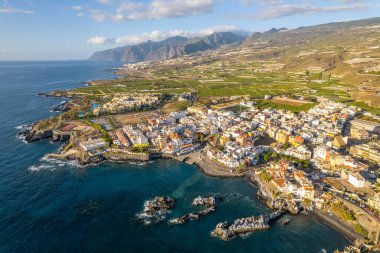 İspanya 'nın Kanarya Adaları, Tenerife' deki resimli Alcala köyünün havadan görünüşü. Geleneksel Kanarya kıyı kasabası, yeşil muz çiftlikleri ve arka planda ünlü Los Gigantes dağları