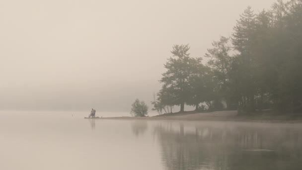 霧の朝に湖岸で釣る人々のシルエット 霧の多い湖が濃い秋の霧の中に消えていく穏やかで最小限の風景 静かで禅のようなシーン — ストック動画