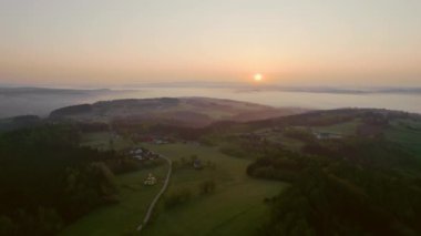 Yaz kırsalının puslu sabah hava manzarası. Gün doğumunda bir köy yolu dağ köyünden geçer. Drone hava görüntüsü