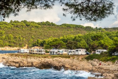 Pula, Hırvatistan - 23 Eylül 2023: Hırvatistan 'ın İstria bölgesi yakınlarındaki Adriyatik Denizi kayalık kıyılarında park halindeki karavanları olan kamp alanı. Aile tatili karavanı, karavanda tatil gezisi.