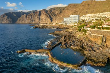 Günbatımında Tenerife adasındaki Los Gigantes manzarası, İspanya. Los Gigantes doğal havuzu, lüks oteller, sahil kenti mimarisi ve görkemli yüksek uçurumlar, Tenerife, Kanarya adaları, İspanya