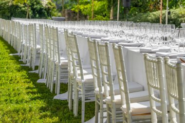 Düğün süslemeleri. Tabaklar, sandalyeler, beyaz peçeteler ve şarap kadehleriyle servis edilen düğün masası. Kutlama detayları, yaz boyunca bahçede açık havada düğün.