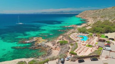 Mallorca, Balearic Adaları, İspanya 'daki çarpıcı Akdeniz kıyılarının hava manzarasında inanılmaz turkuvaz suları, demirli bir yelkenli ve yüzme havuzlu lüks bir sahil barı var..