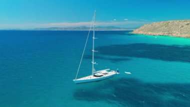 Güzel, modern bir yelkenli, İspanya 'nın Balear Adaları, Mallorca' daki Akdeniz 'in inanılmaz turkuaz sularında demirlemiştir. Drone yörünge atışı. Yatçılık, seyahat ve aktif yaşam tarzı konsepti