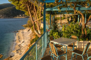 Traditional outdoor Greek restaurant on the beautiful Mediterranean sea coast in Agia Effimia village, Kefalonia, Ionian Islands, Greece. Empty terrace without people at sunset clipart