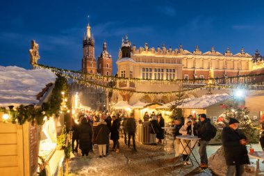 Krakow, Polonya - 5 Aralık 2024: Polonya 'nın Krakow kentindeki Ana Pazar Meydanı' nda geleneksel Noel fuarları. Güzel bir Noel tezgahı ve tatil aydınlatması. Krakow 'daki Mariacki Kilisesi ve Kumaş Salonu