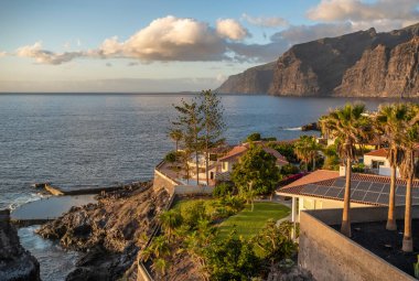 İspanya, Tenerife 'de günbatımında Acantilados de Los Gigantes' te palmiye ağaçları olan lüks villalar. Tenerife Adası 'ndaki Los Gigantes tatil köyünün güzel manzarası.