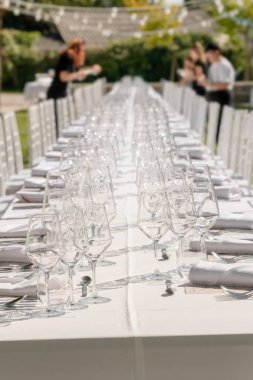 Düğün süslemeleri. Tabaklar, sandalyeler, beyaz peçeteler ve şarap kadehleriyle servis edilen düğün masası. Kutlama detayları, yaz boyunca bahçede açık havada düğün. Seçici odak