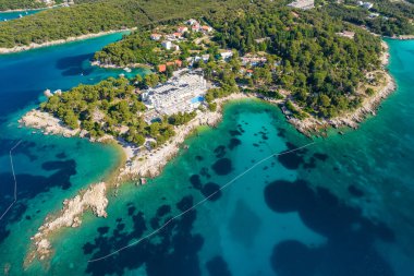 Hırvatistan 'ın Rab adasında Adriyatik Denizi' nin muhteşem mavi ve turkuaz renkleriyle güzel suları var. Kristal berrak deniz suyuyla kaplı kayalık bir sahile kurulmuş lüks tesisin hava manzarası.