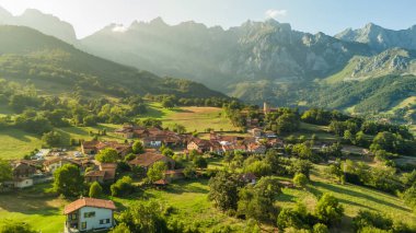 Kuzey İspanya, Cantabria 'daki Mogrovejo ortaçağ köyünün havadan görünüşü. Geleneksel evler, tarihi bir ortaçağ kulesi ve yazın Picos de Europa dağlarının görkemli zirveleri..
