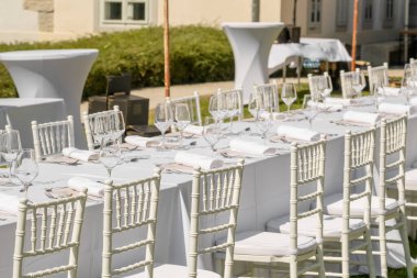 Düğün süslemeleri. Tabaklar, sandalyeler, beyaz peçeteler ve şarap kadehleriyle servis edilen düğün masası. Kutlama detayları, yaz boyunca bahçede açık havada düğün.