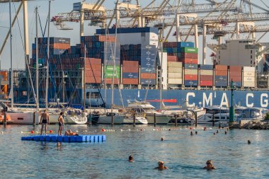 Koper, Slovenya - 17 Eylül 2023: Slovenya 'nın Koper limanında yüzen kimliği belirsiz kişiler, arka planda demirlemiş büyük bir kargo tankeri ile.