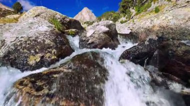 Buzuldan gelen temiz bir su akıntısı taş kayaların arasından ağır çekimde geçiyor. Aragon, İspanya 'daki Pirenes dağlarındaki Benasque vadisindeki Aigualluts uçaklarının güzel manzarası.