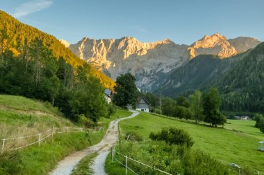 Slovenya 'nın Zgornje Jezersko kentinde gün batımında Kamnik-Savinja Alpleri tarafından çerçevelenen Ravenska Kocna Vadisi' nden geçen bir kır yolu ile Idyllic kırsal arazisi