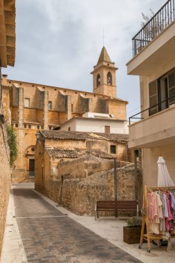 İspanya, Balearic Adaları, Mallorca 'daki sevimli Santanyi kasabası. Pedestrian caddesinde butik dükkanları ve kafeleri var. Arka planda tarihi Sant Andreu de Santanyi kilisesi var..