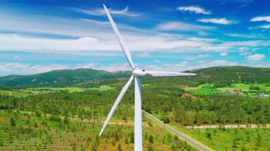 Dağın tepesinde dönen bıçakları olan büyük beyaz rüzgar türbinlerinin havadan görüntüsü. Rüzgar enerjisi, güneşli bir yaz gününde kendine yeten çevre dostu elektrik üretiyor..