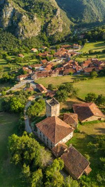 Kuzey İspanya, Cantabria 'daki Mogrovejo ortaçağ köyünün havadan görünüşü. Geleneksel evler, tarihi bir ortaçağ kulesi ve yazın Picos de Europa dağlarının görkemli zirveleri..