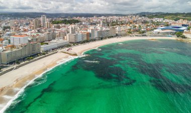 A Coruna, Galiçya, İspanya 'da güneşli bir günde Playa del Orzan plajının hava manzarası. Şehir merkezinde canlı turkuaz deniz suyuyla dolu uzun kumlu bir sahil. Kuzey İspanya 'da halk seyahati