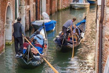 Venedik, İtalya - 11 Ekim 2024: Venedikli gondolcu Venedik, İtalya 'da dar bir kanal boyunca turistlerle gondolda yolculuk ediyor.
