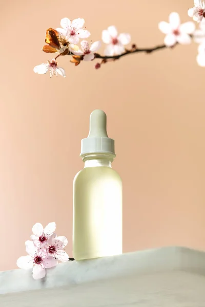 White glass dropper bottle with white lid on white marble shelf, natural spring background. SPA natural organic beauty product packaging design, branding. Beauty salon mockup, low angle view, below