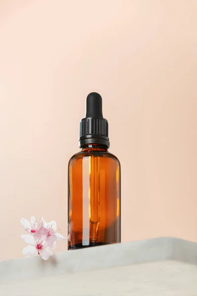 Amber glass dropper bottle with black lid on white marble shelf, natural spring background. SPA natural organic beauty product packaging design, branding. Beauty salon mockup, low angle view, below