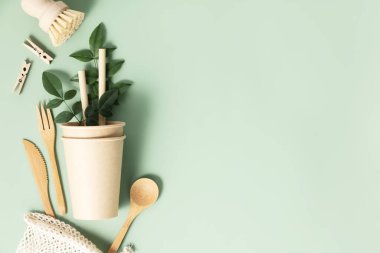 Açık yeşil arka planda sofra takımı olan eko kompozisyonu. Eko doğal kağıt bardaklar, bambu çatal bıçaklar ve yeşil yapraklar düz fotokopi alanı oluşturur