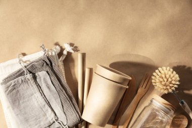 Yeniden kullanılabilir çevre dostu ürünler. Sıfır atık. Eko doğal kağıt bardaklar, bambu çatal bıçak takımı, doğal temizlik ürünleri, doğal bej kağıt arka planda yeniden kullanılabilir pamuk torbaları, düz yatak. Plastik