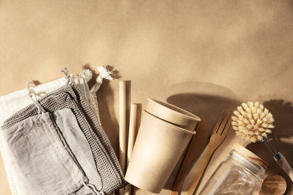 Set of reusable eco friendly products . Zero waste concept. Eco natural paper cups, bamboo cutlery, natural cleaning products, reusable cotton bags on natural beige paper background, flat lay. Plastic