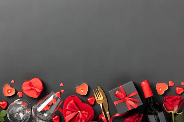 Beautiful romantic table setting with wine, roses and gifts on black background. Romantic dinner. Valentines Day. Top view, flat lay, copy space