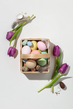Easter composition with Pink tulips and basket with eggs on white background flat lay, top view